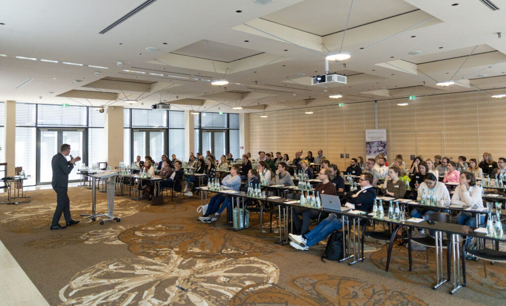 Vortragsraum im Atrium Hotel in Mainz. Personen sitzen an Tischen und hören dem Vortrag zu