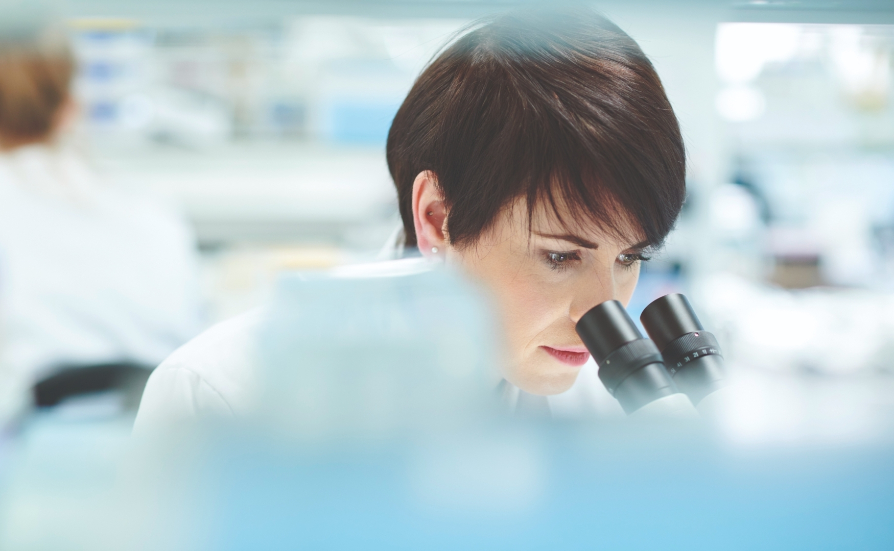 Wissenschaftlerin bei der Qualitätskontrolle im Labor, blickt konzentriert durch ein Mikroskop – Symbolbild für pharmazeutische Forschung und zertifizierte Sicherheit bei Medinoxx